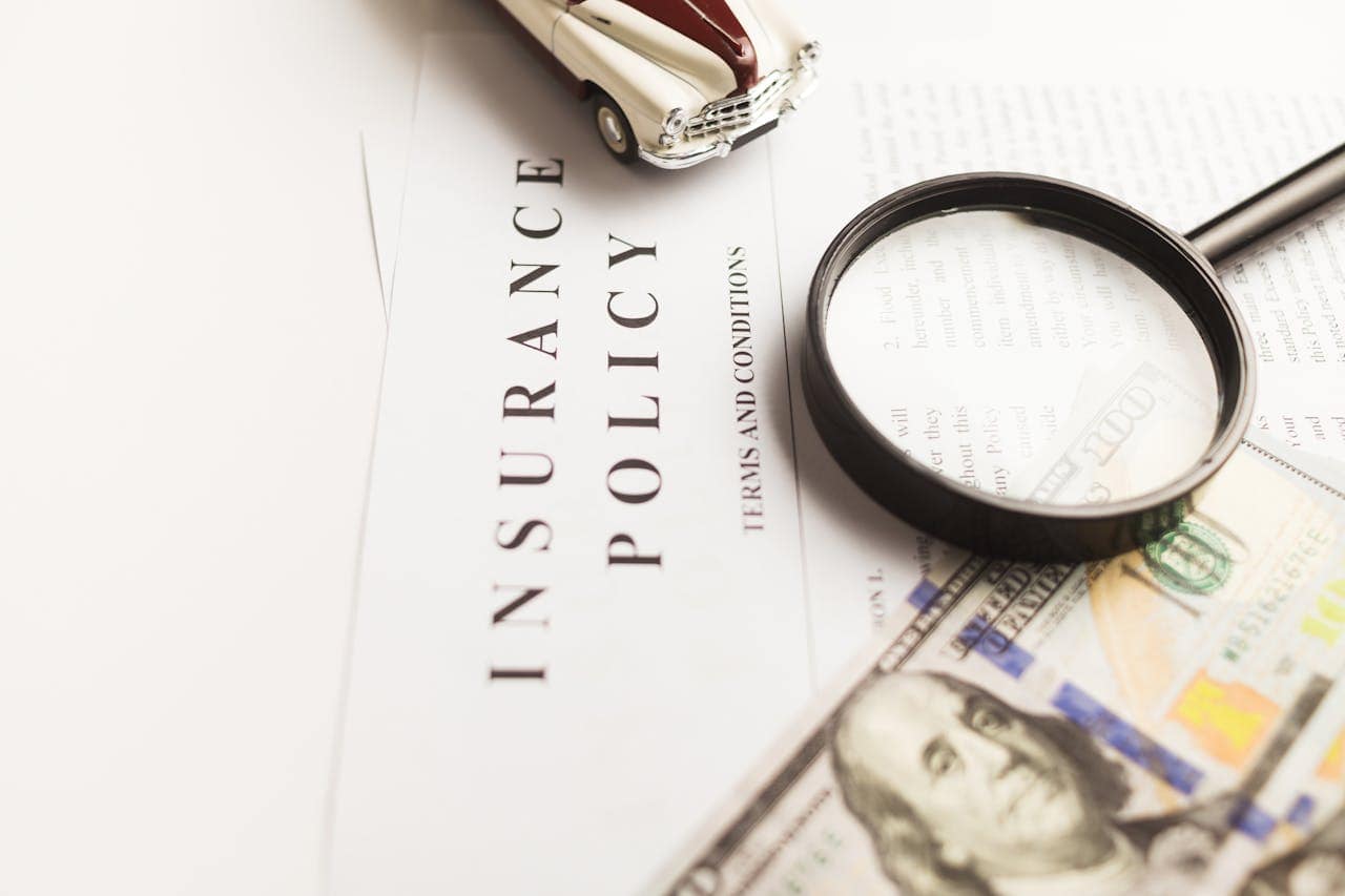 Insurance Policy Document with Magnifying Glass and Model Car, representing risk management. Insurance policy document with magnifying glass, model car, and money, highlighting insurance and risk management.