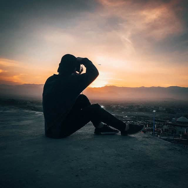 Person sitting on rooftop during sunset, gazing at the horizon.